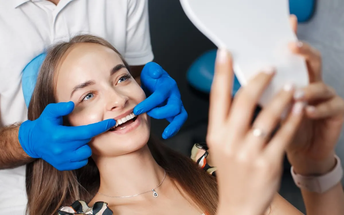 A smiling dental patient checking her new smile in a mirror in Istanbul