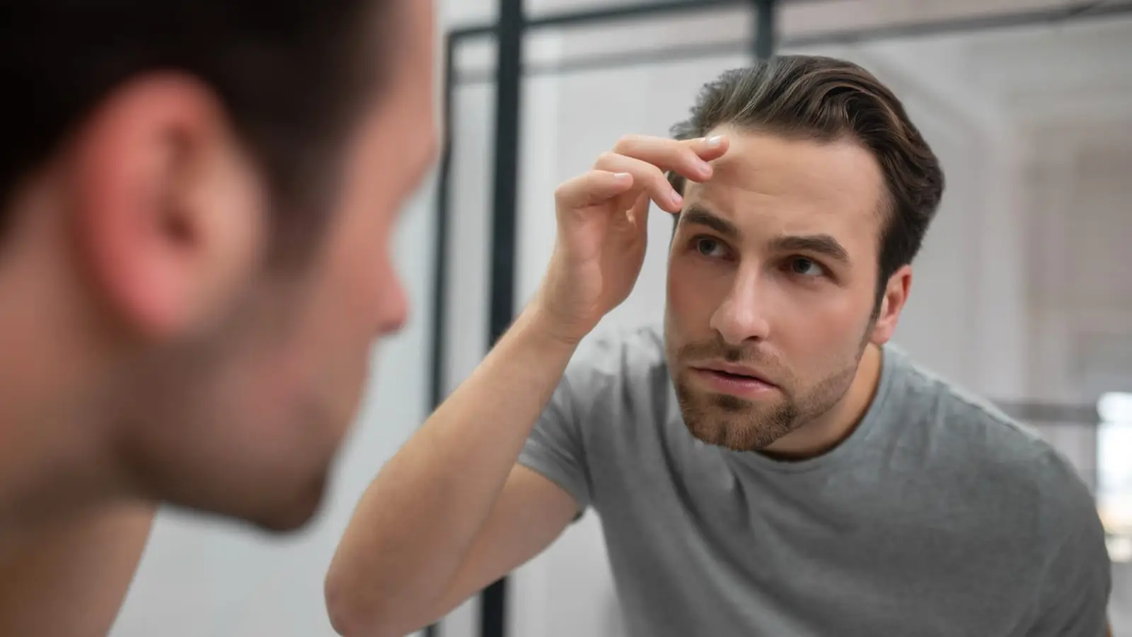 A man examining his hairline in a mirror while considering a hair transplant in Turkey