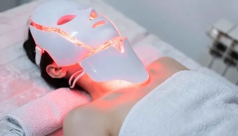 Mujer usando en casa una mascarilla facial de fototerapia LED